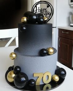 a black and silver cake with gold decorations on it's top, sitting on a table