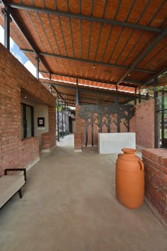 an orange vase sitting on top of a cement floor next to a brick wall and bench