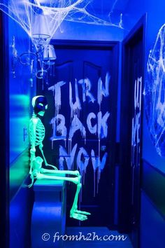 a room with neon blue walls and ghost decorations on the door, in front of an open doorway that says turn back now