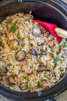 rice and mushrooms are in the crock pot with a red spatula on top