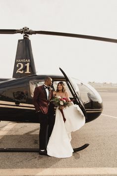 a bride and groom standing in front of a helicopter on the tarmac at an airport