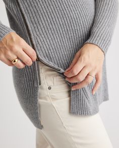 a woman in white pants and a gray sweater is holding her hand on her hip