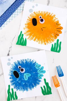 two handprinted pictures of blue and orange sea creatures on white paper with forks