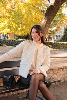 a woman sitting on top of a wooden bench next to a tree in the park