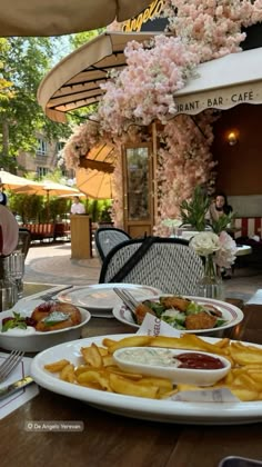 plates of food are sitting on a table outside at an outdoor restaurant with flowers in the background