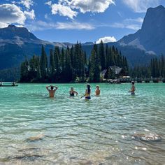 several people are swimming in the water near some mountains and pine trees with blue sky