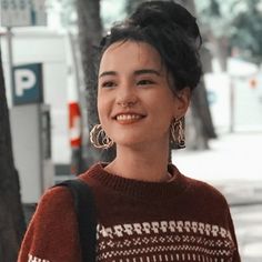 a woman standing next to a tree on a sidewalk with her hand in her pocket