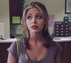 a young woman is staring at something in the distance while standing in front of a desk