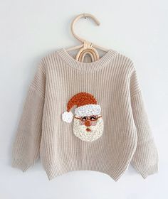 a sweater with a santa clause on it hanging from a wooden hanger against a white wall