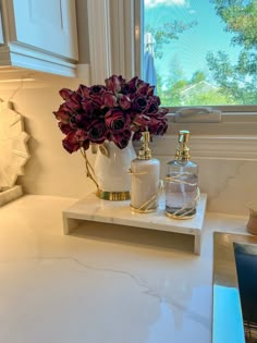 a white counter top with two bottles and flowers on it in front of a window