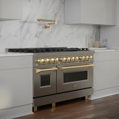 a kitchen with marble counter tops and stainless steel ovens, gold pulls on the hood