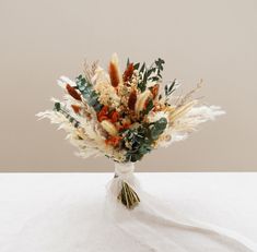 an arrangement of dried flowers and foliage in a vase on a tablecloth covered surface