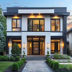 a white and black house with lots of windows in the front yard at night time