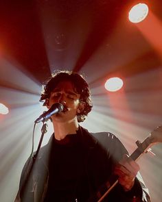 a man holding a guitar while standing in front of a microphone on top of a stage