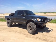 a black truck parked on top of a dirt road next to a body of water