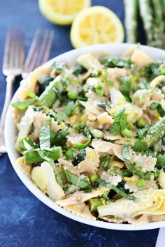 a white bowl filled with pasta and asparagus next to lemon wedged asparagus