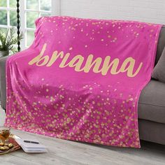 a pink and gold blanket with the word branna on it sitting on a couch