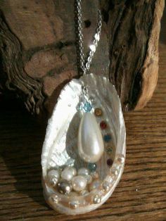 a white necklace with pearls and a tear shaped pendant on a wooden table next to a piece of driftwood