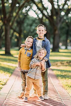 three young boys are standing together on a brick path in front of trees and grass