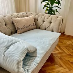 a blue and white checkered couch with a pillow on it's back next to a potted plant