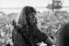 a black and white photo of a woman holding a guitar in front of an audience