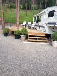 a camper parked in the woods next to some plants and trees with chairs around it