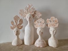 three ceramic figurines with leaves on their heads