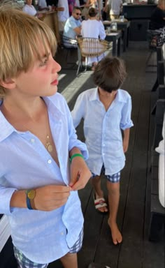 two young boys standing next to each other in front of tables with people sitting at them