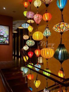 many colorful lanterns hanging from the ceiling in a room with stairs and paintings on the wall