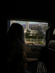 a woman sitting in the passenger seat of a car at night with her hand on the steering wheel