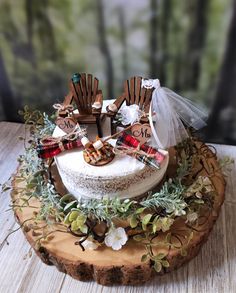 a wedding cake decorated with wooden chairs and greenery on a wood slice, sitting on a table