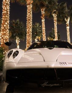 a white sports car parked in front of palm trees with lights on it's sides