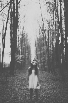 a woman standing in the middle of a forest wearing a deer headdress and scarf