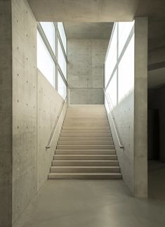 an empty staircase leading up to the second floor in a building with concrete walls and windows