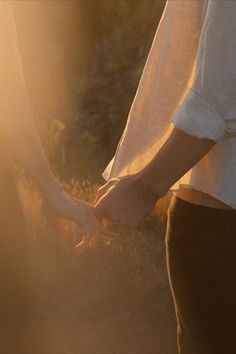 two people holding hands while standing next to each other with the sun shining on them