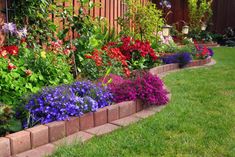 a garden filled with lots of colorful flowers next to a wooden fence and green grass