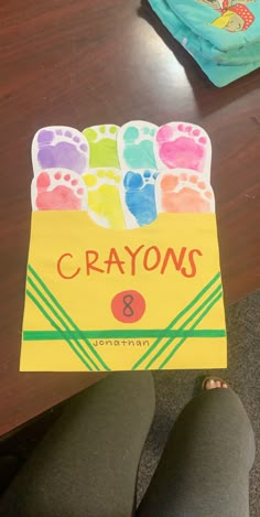 a child's hand holding up a crayons book with their feet on the table