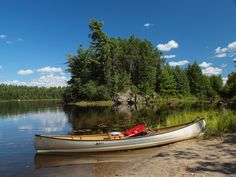 a canoe sitting on the shore of a lake with trees in the background and blue sky