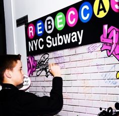 a young man writing on a brick wall with colorful stickers and graffiti in front of him