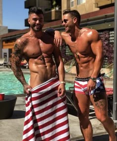 two men standing next to each other in front of a swimming pool with an american flag towel draped around them