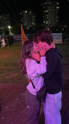 a man and woman kissing in front of a cityscape at night with the lights on