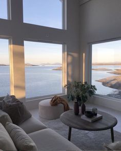 a living room filled with furniture and large windows looking out onto the water at sunset