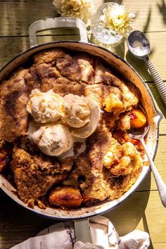 an apple cobbler with ice cream on top sits on a wooden table next to flowers