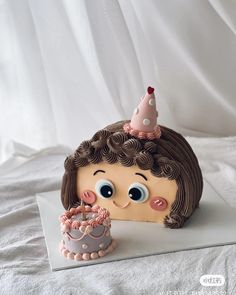 a cake shaped like a girl with a birthday hat on it's head and a cupcake in front of her