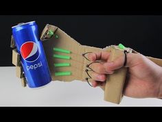 a hand is holding a soda can in front of a cardboard structure