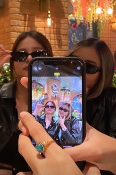 two women are taking pictures with their cell phones while sitting at a table in front of them