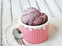 a pink bowl filled with ice cream sitting on top of a white plate next to a spoon