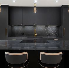 two bar stools sit in front of an island with marble countertops and black cabinets