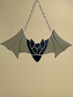 a stained glass bat hanging from a chain in the shape of a heart on a beige wall