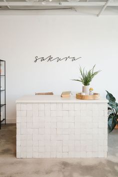 a white counter with some plants on it in front of a wall that says sakrara